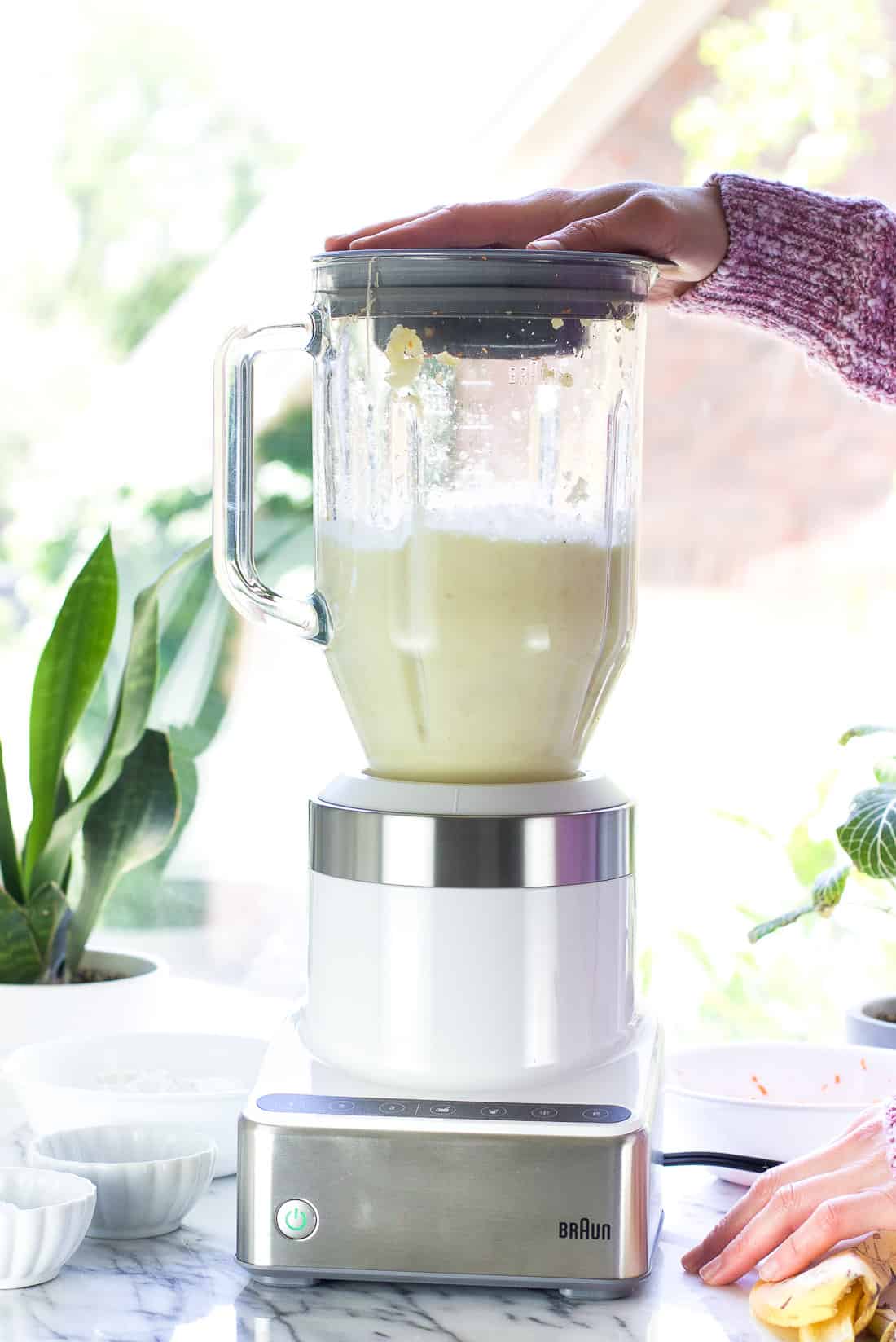 Pancake batter being mixed in a blender, with a woman's hand holding onto the top of the blender