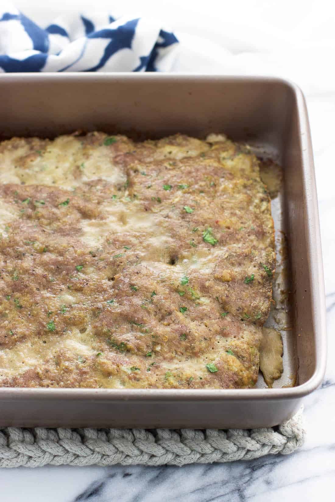 A flat layer of baked turkey meatball mixture in a square pan.