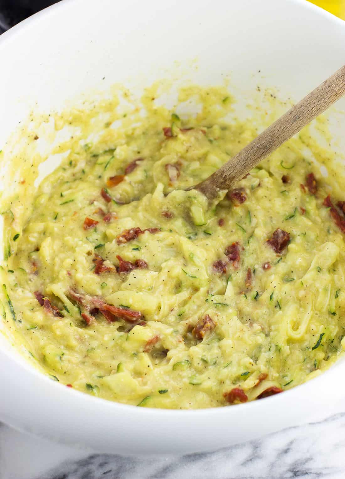 Quiche mixture stirred together in a plastic mixing bowl with a wooden spoon