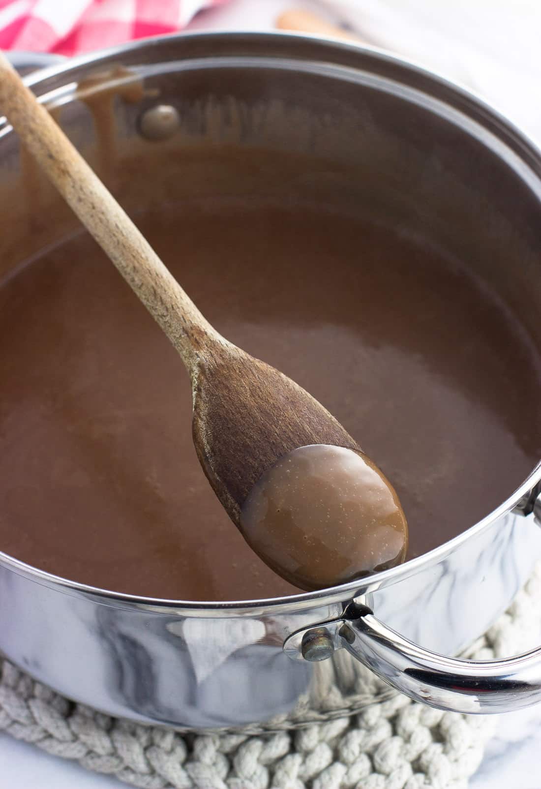 The fudgesicle mixture in a saucepan with a wooden spoon lifted out to show the mixture coating the back of it in a thick layer