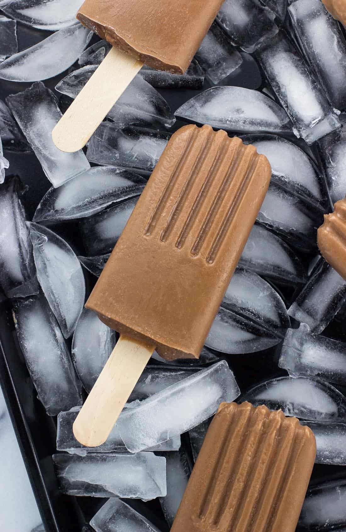 Several fudge popsicles on a tray of ice cubes