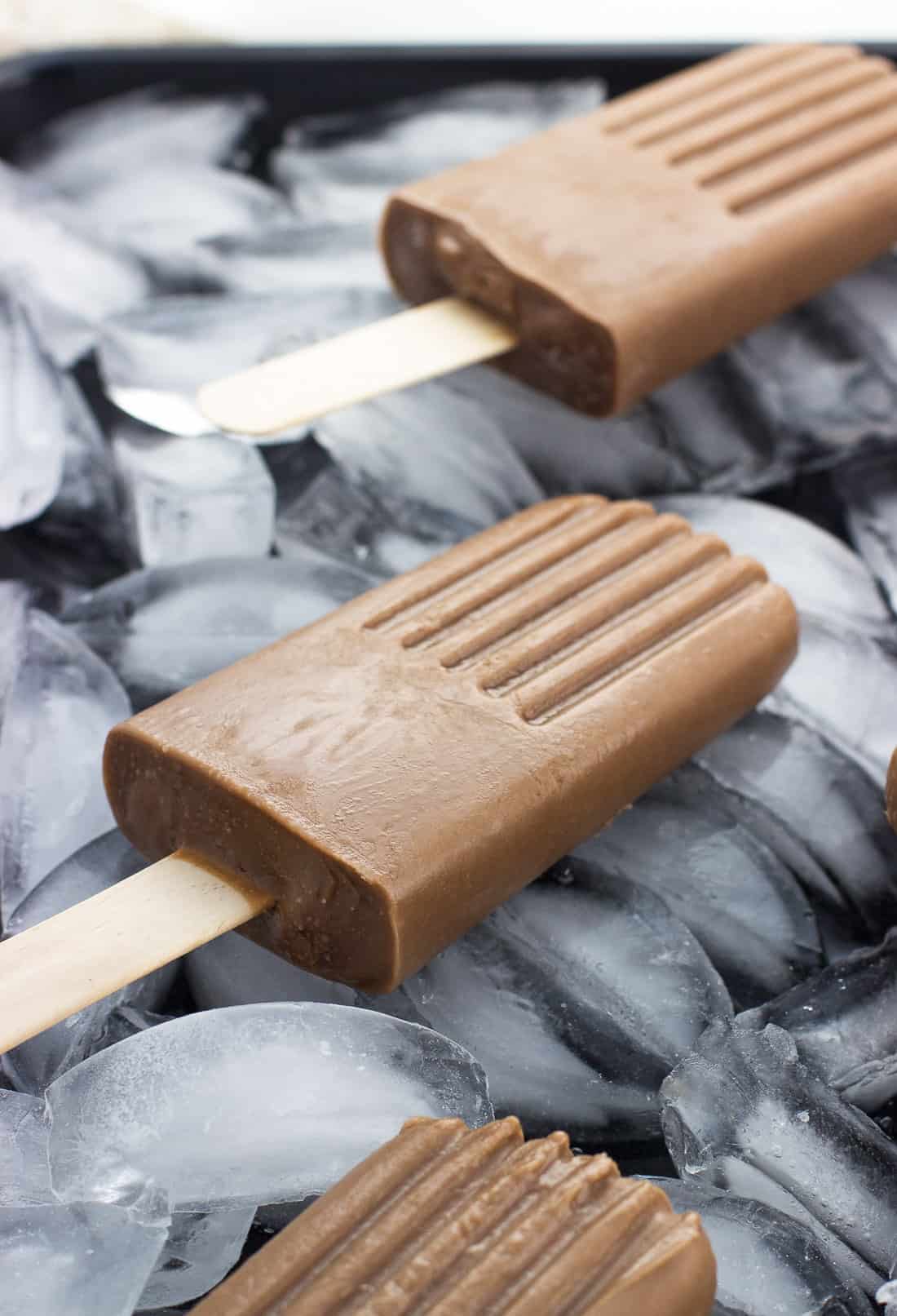 A side view of a chocolate fudge pop on a bed of ice