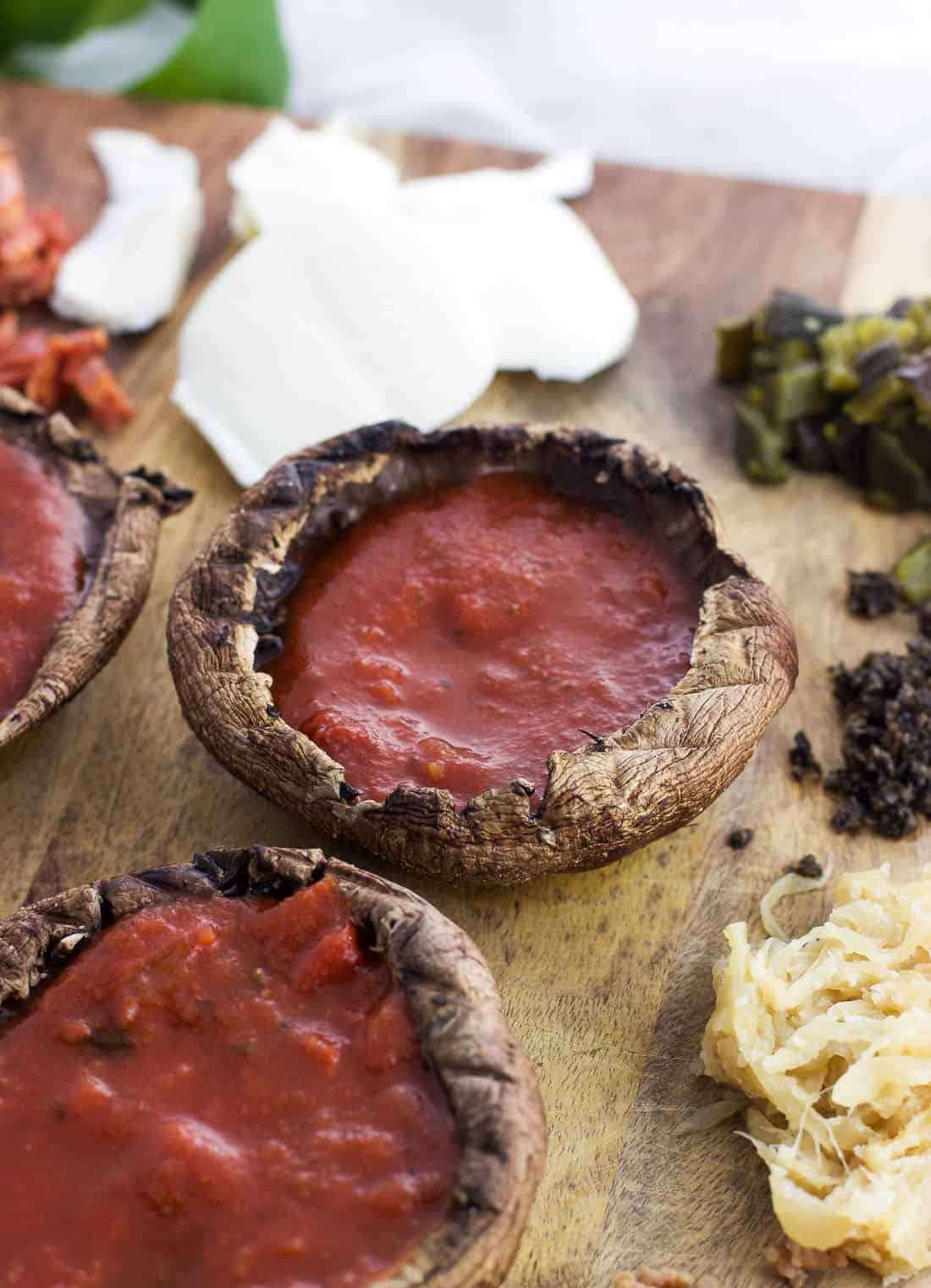 Portobello mushroom caps filled with pizza sauce before adding the other toppings.