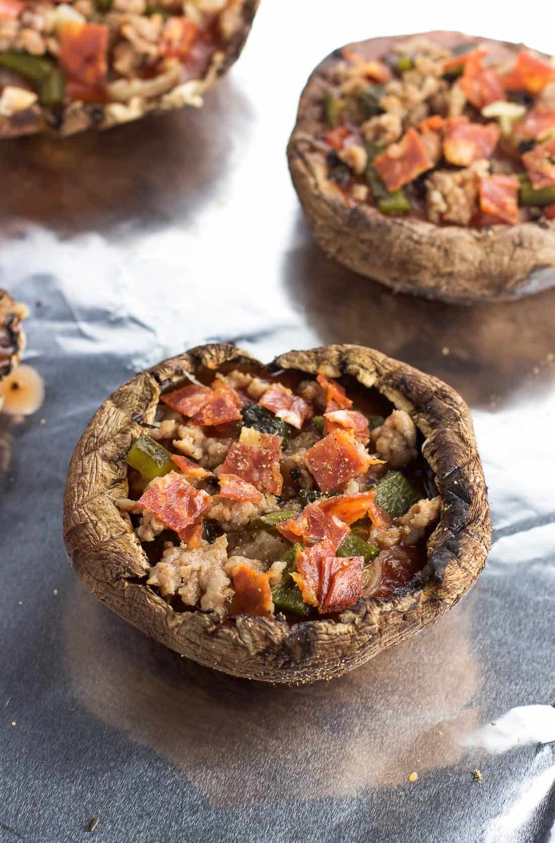 Portobello caps on a baking sheet stuffed with pizza sauce and toppings before adding cheese.