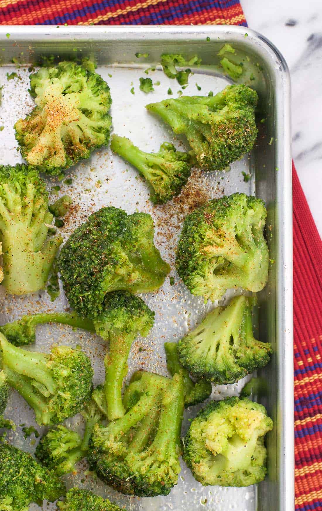 Broccoli florets on a rimmed baking sheet after being tossed in olive oil and seasoned before roasting