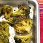 Broccoli florets on a rimmed metal baking sheet roasted and seasoned with Cajun and garlic seasonings