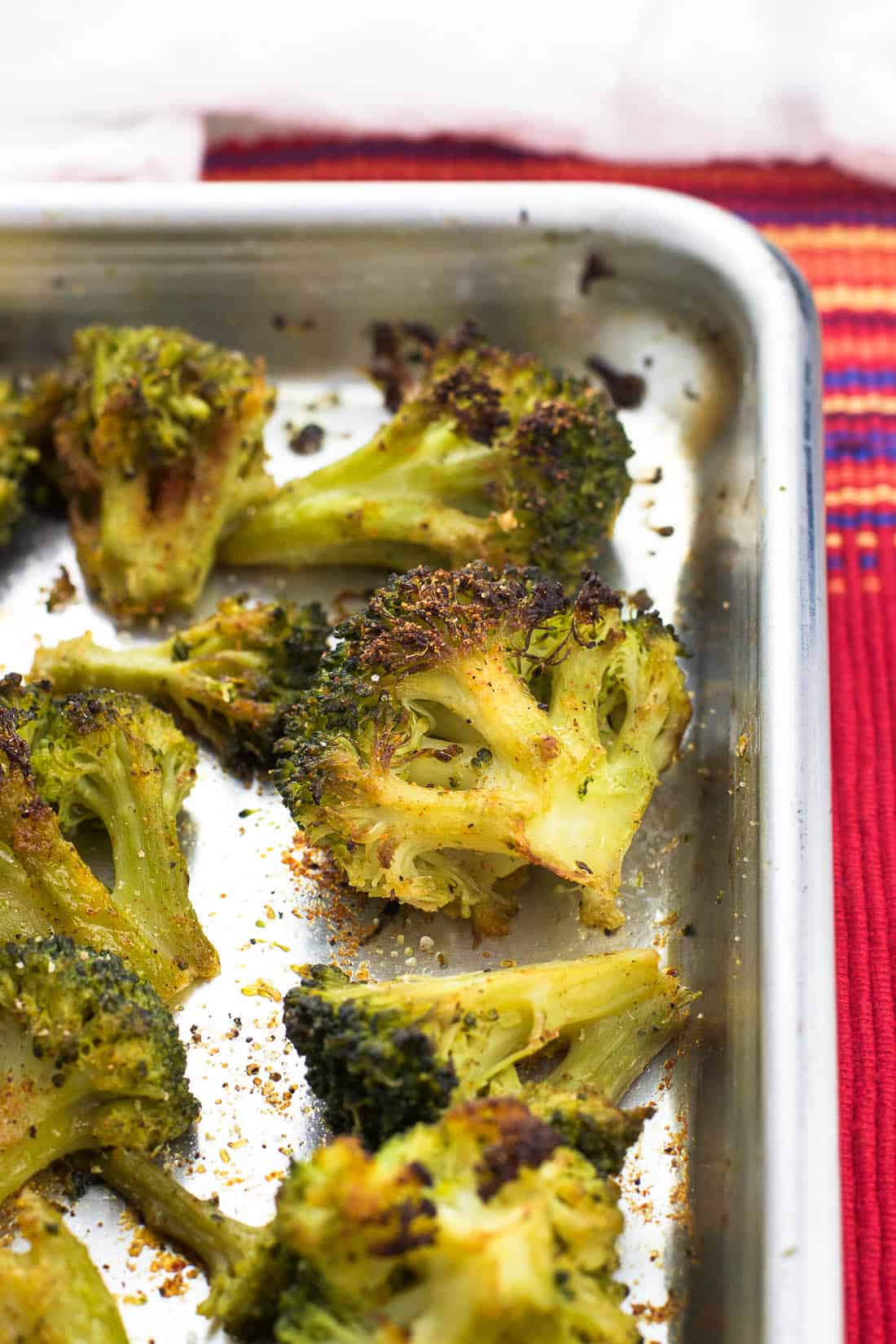 Broccoli florets on a rimmed metal baking sheet roasted and seasoned with Cajun and garlic seasonings