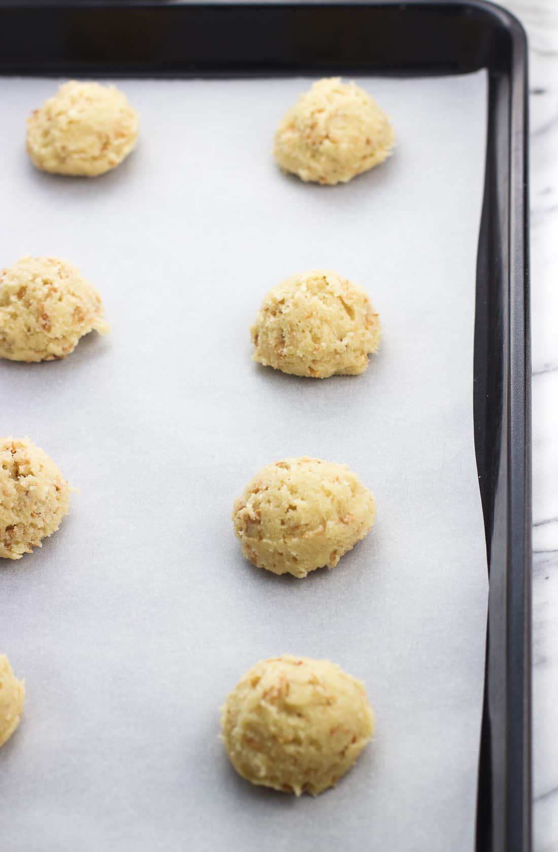 Raw cookie dough scooped onto a parchment-lined baking sheet.