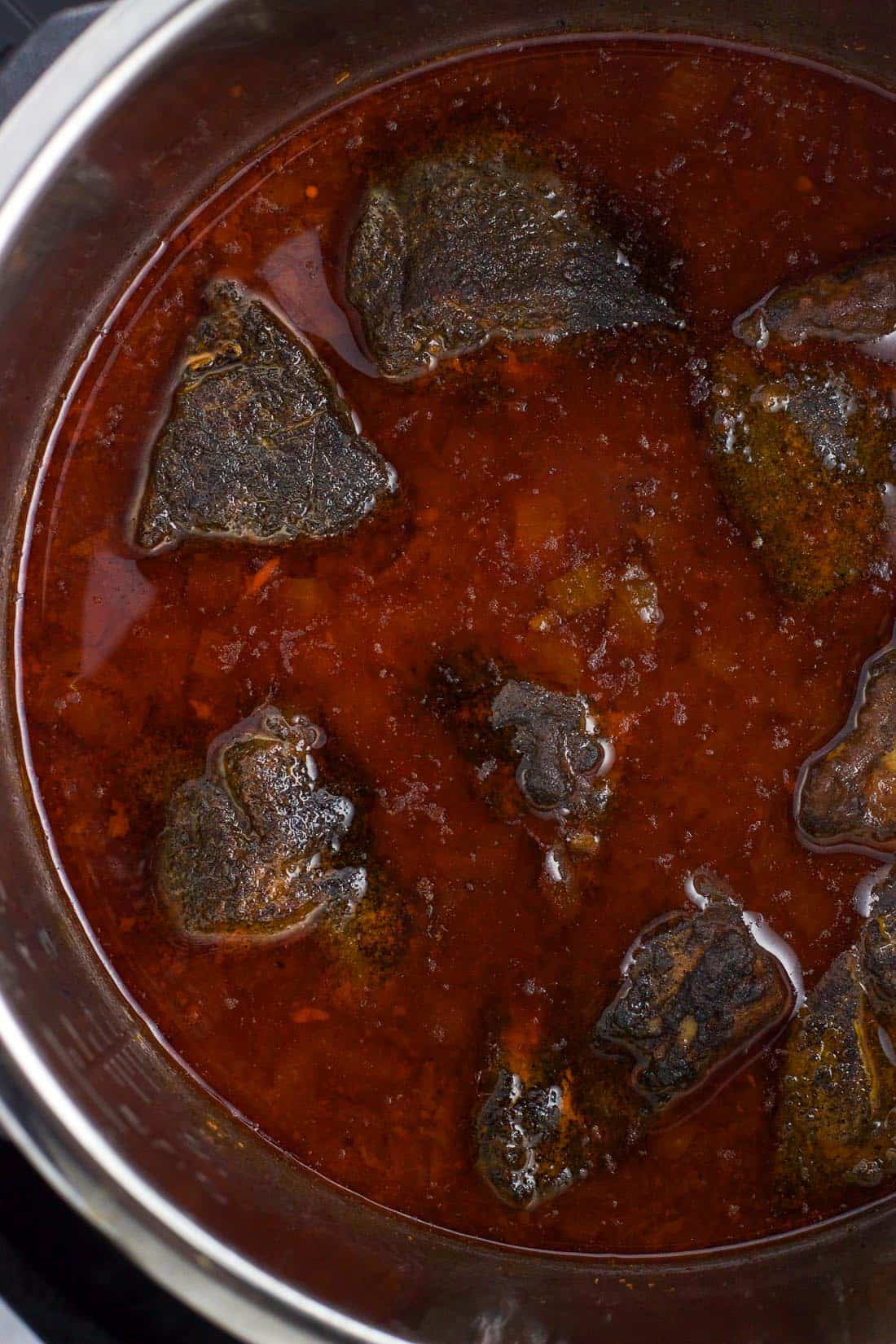 An overhead picture of cooked pork chunks in cooking liquid before thickening it into BBQ sauce.