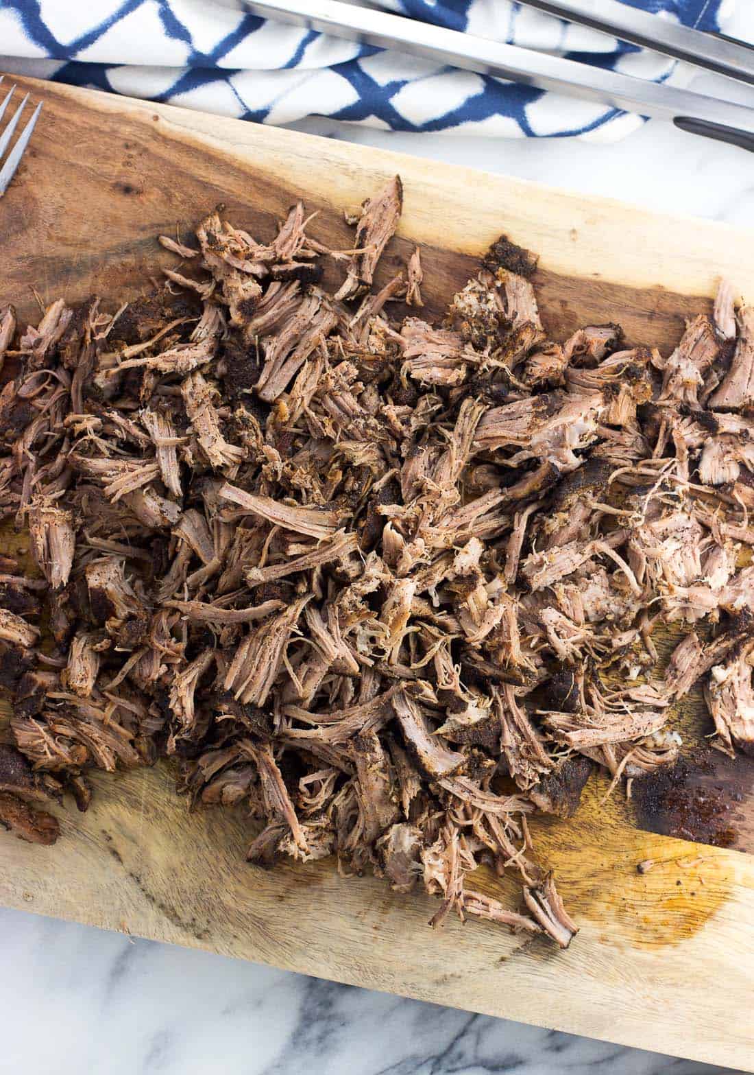 An overhead picture of shredded pulled pork on a wooden cutting board