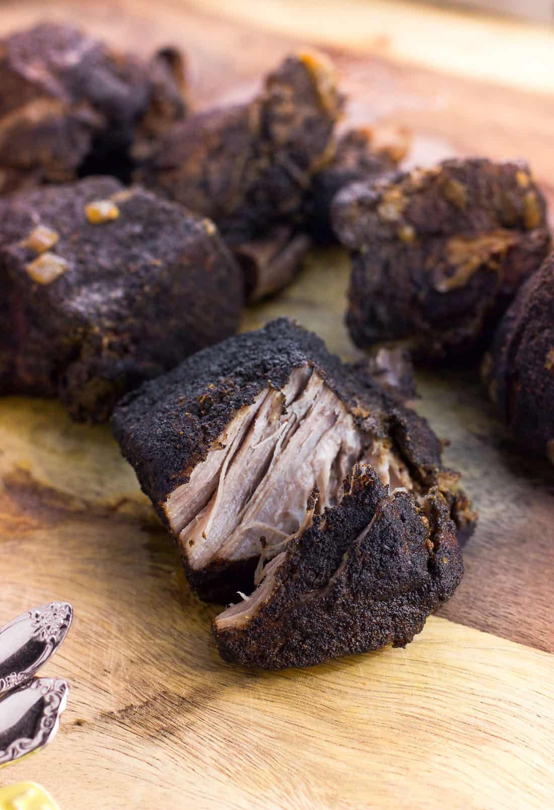 Pieces of coffee rubbed pork on a wooden cutting board with the front piece cut in half.