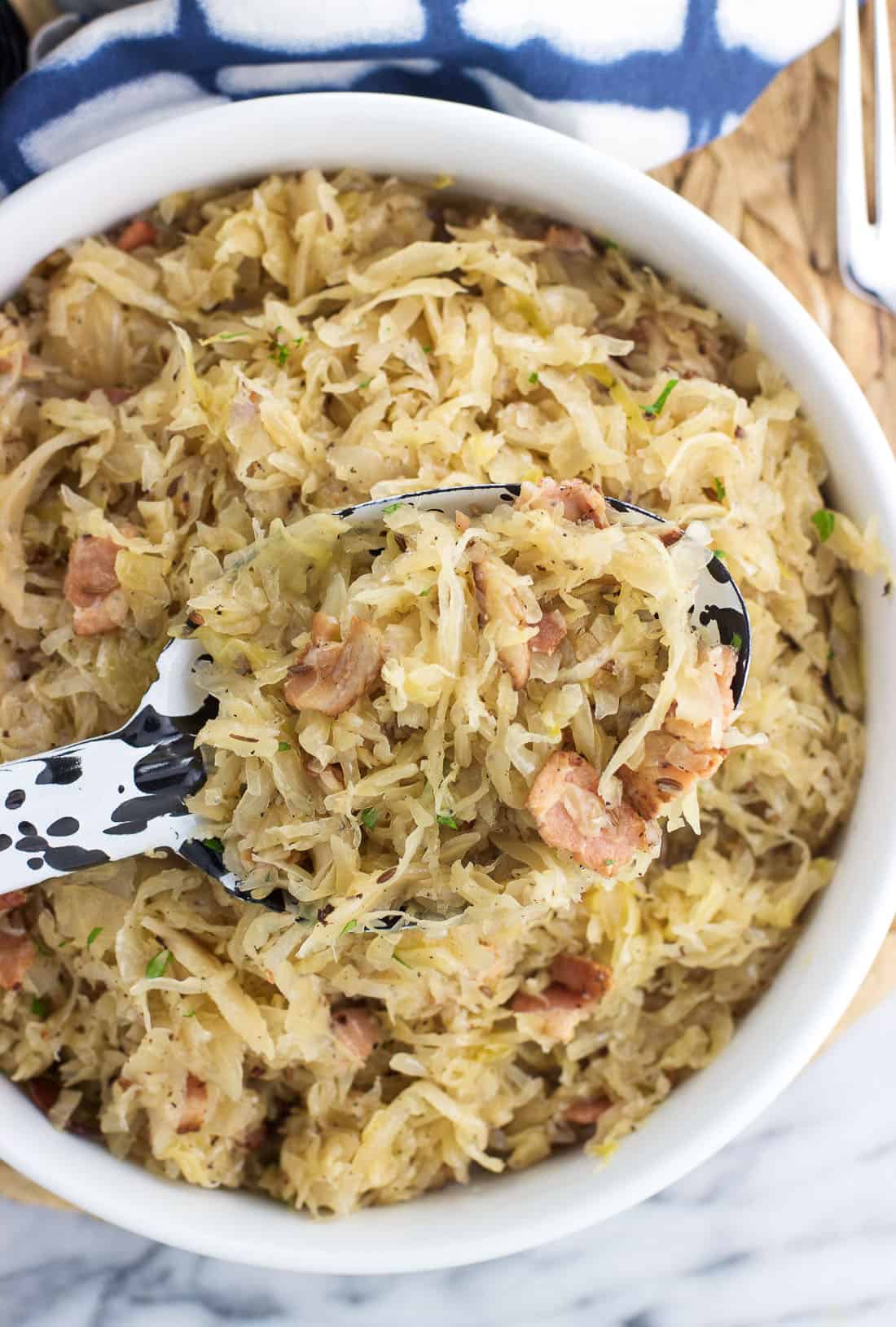 A serving spoon dipped into a bowl of sauerkraut.