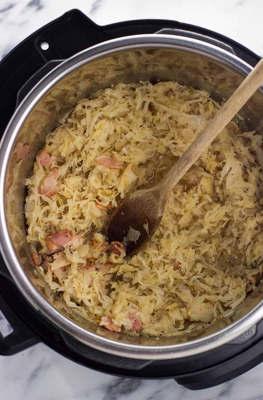 Cooked sauerkraut in the Instant Pot with a wooden spoon.