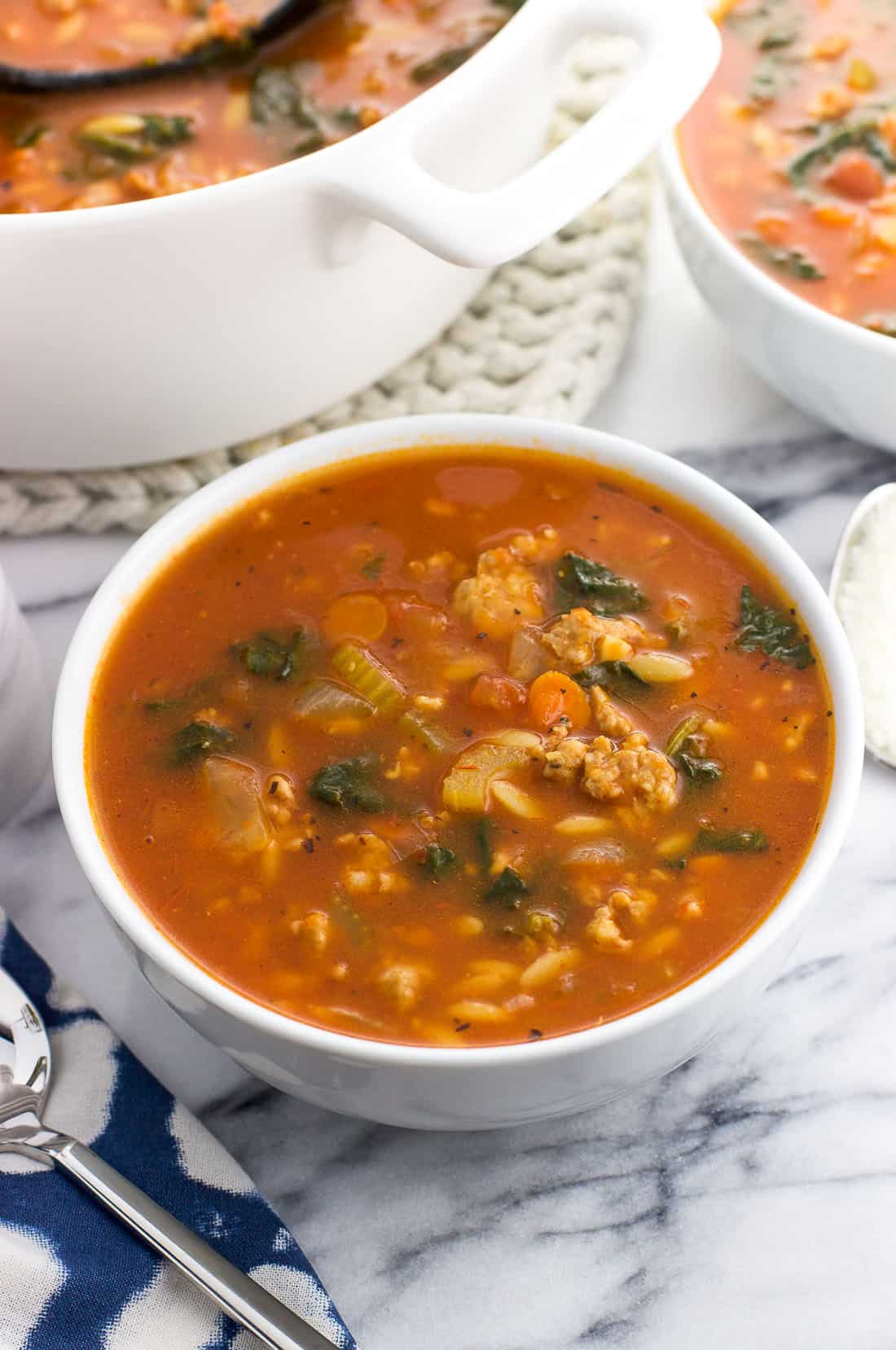 Una ciotola di zuppa di salsiccia davanti a un'altra ciotola e al pentolone di zuppa