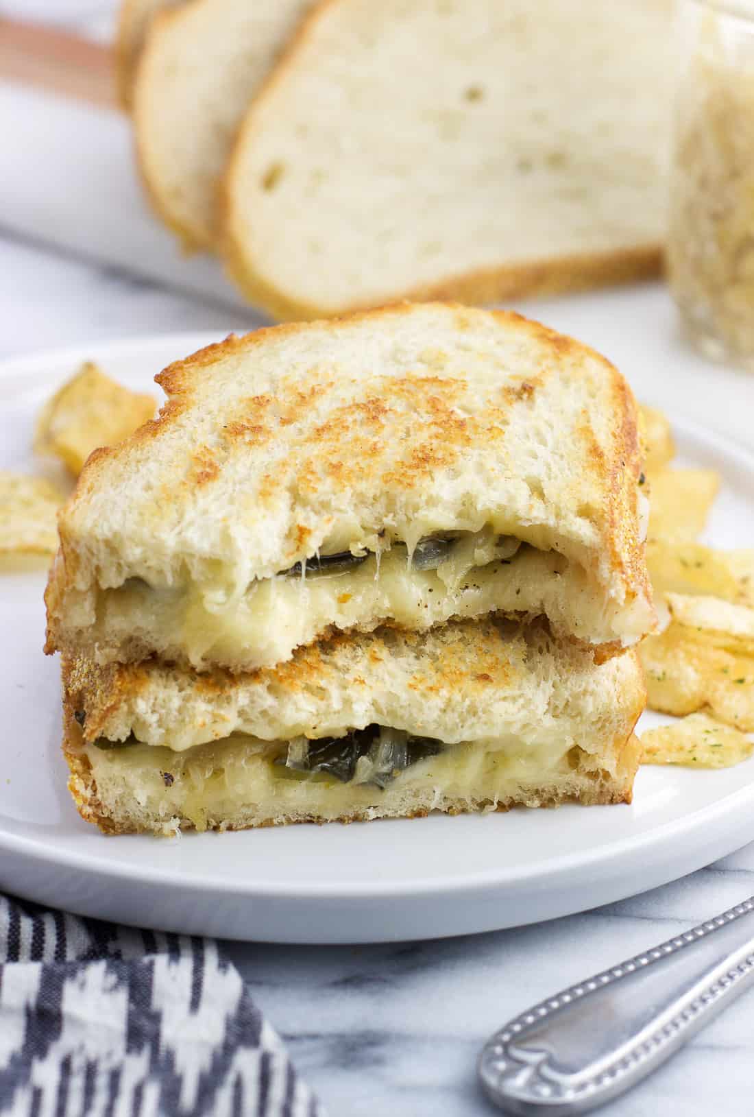 Two halves of a havarti grilled cheese stacked on top of one another with potato chips on a plate