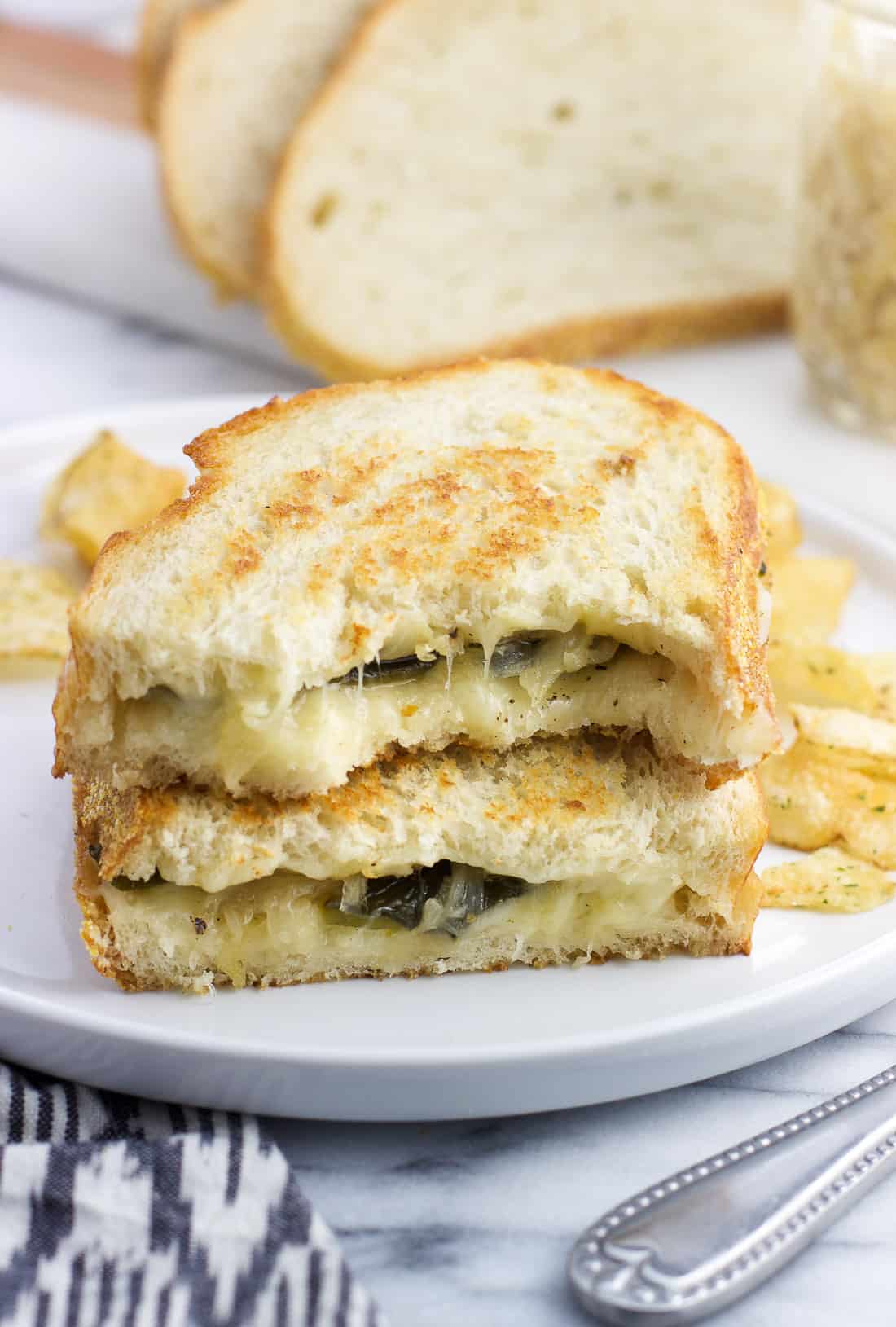 Two halves of a havarti grilled cheese stacked on top of one another with potato chips on a plate.