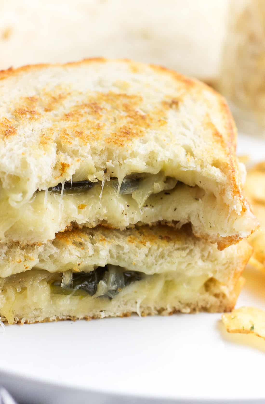 A close-up of two stacked halves of a grilled cheese sandwich showing the melty peppers and onion filling.