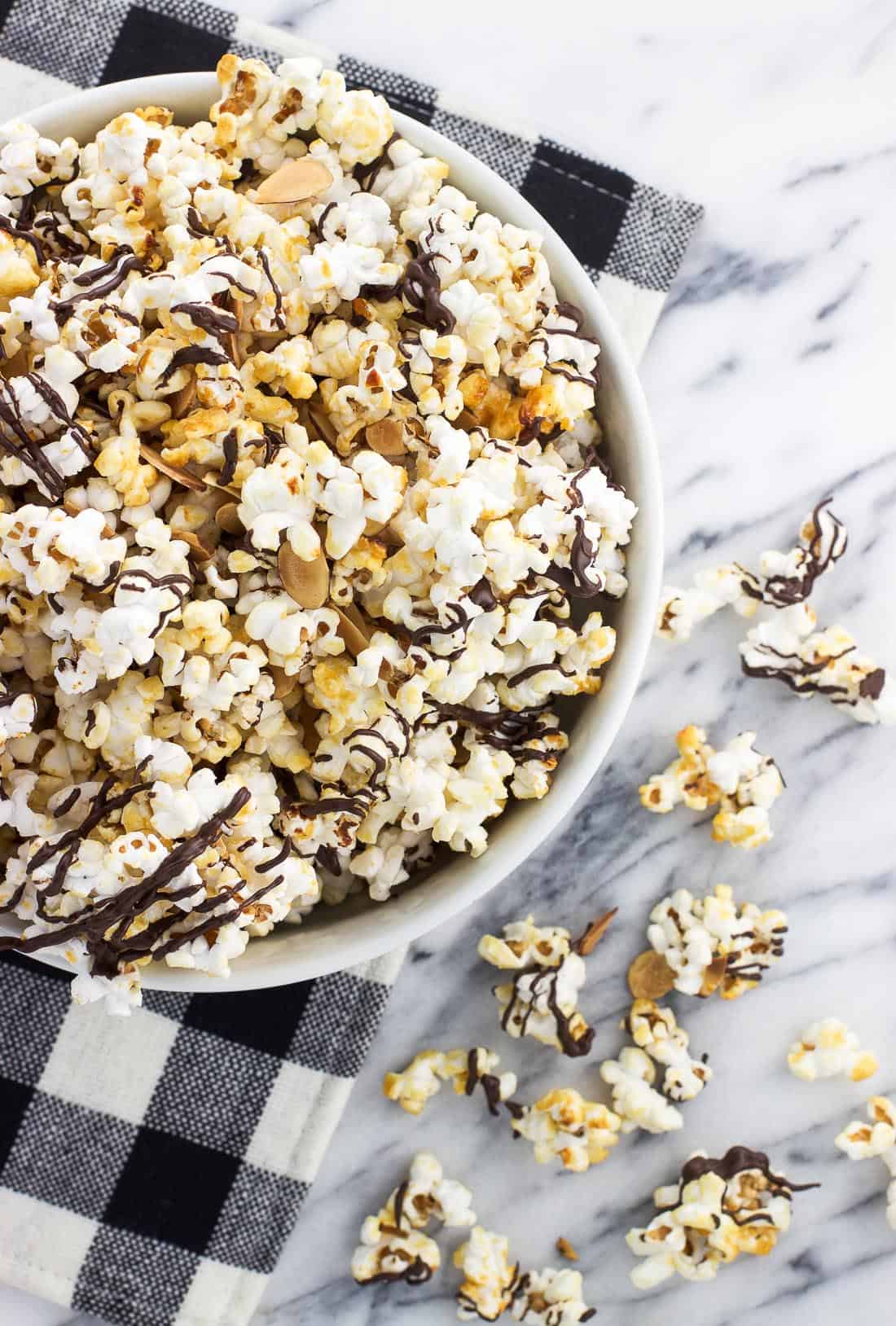 A bowl of chocolate kettle corn on a marble board with some loose kernels and clusters next to it
