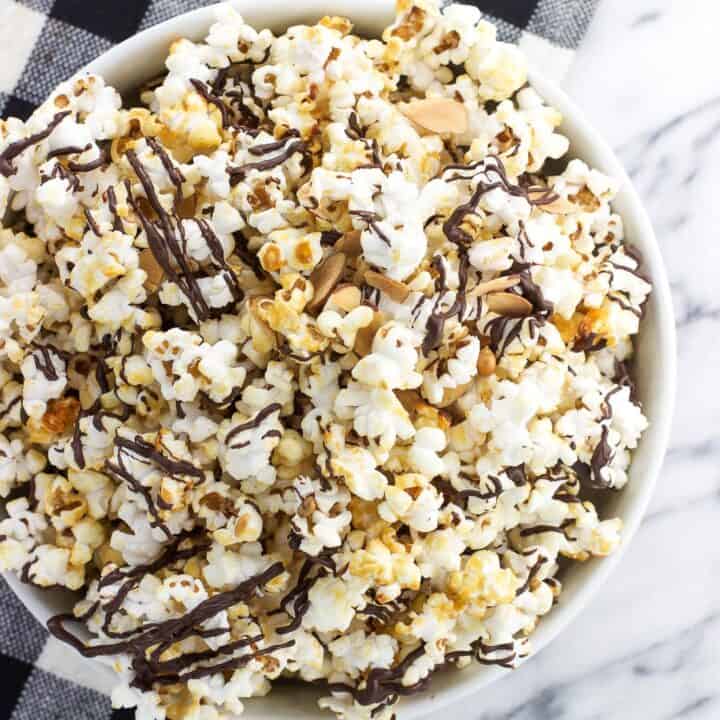 A bowl of chocolate drizzled kettle corn in a low ceramic bowl