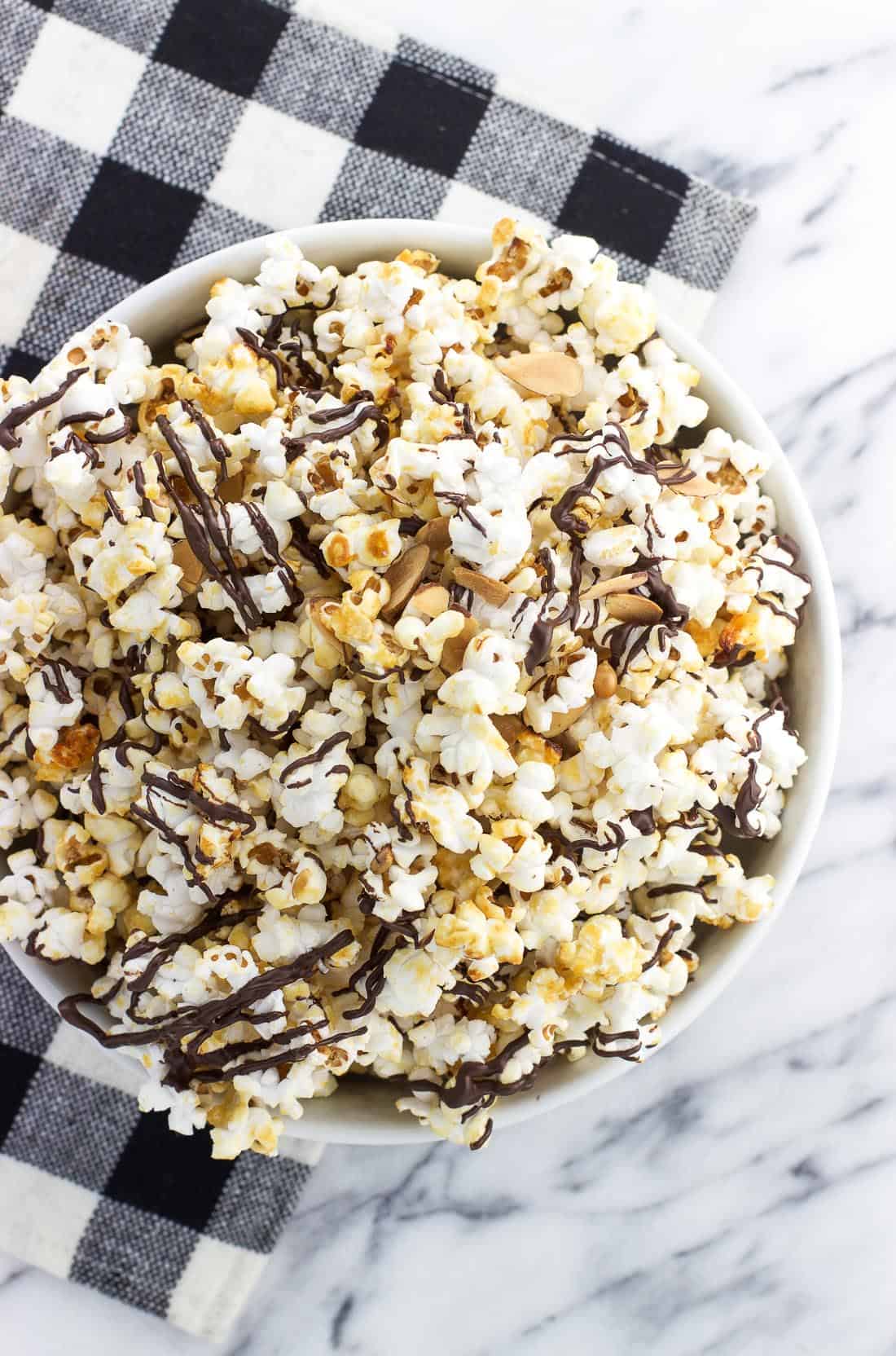 An overhead view of a ceramic bowl of kettle corn next to a buffalo check placemat