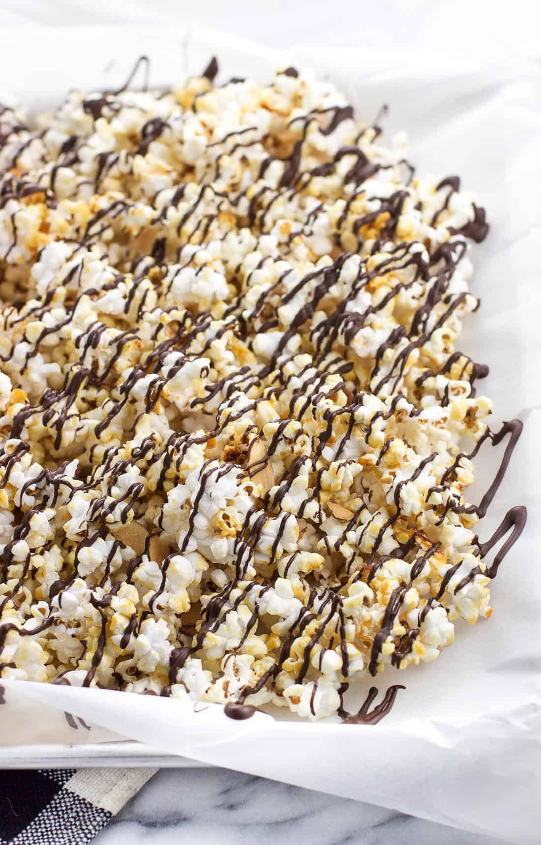 Kettle corn spread out on parchment freshly drizzled with melted dark chocolate