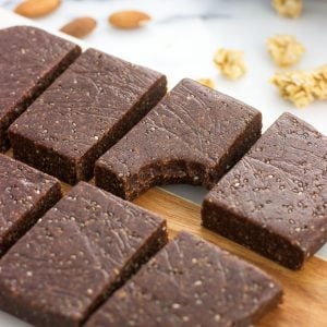 Trail mix bars on a serving board with a bite taken out of one. Almonds and granola clusters are on the board in the background