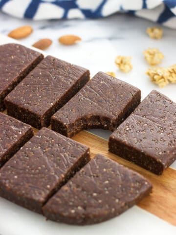 Trail mix bars on a serving board with a bite taken out of one. Almonds and granola clusters are on the board in the background