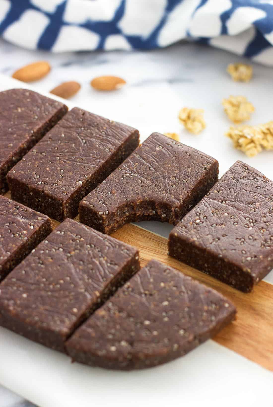 Trail mix bars on a serving board with a bite taken out of one. Almonds and granola clusters are on the board in the background