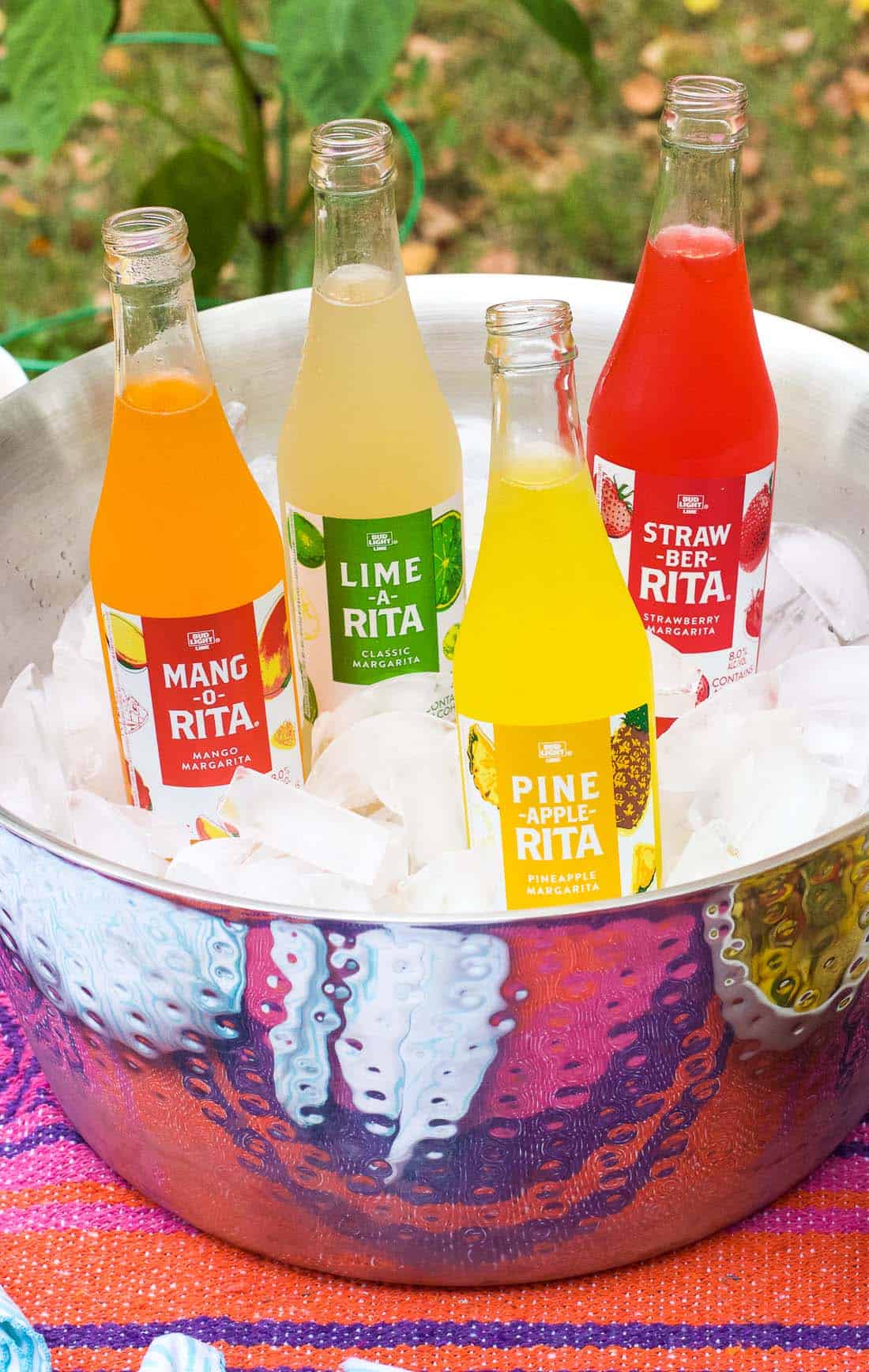 Four bottles of RITAs (mango, lime, pineapple, and strawberry) in an ice cube-filled hammered metal cooler bucket