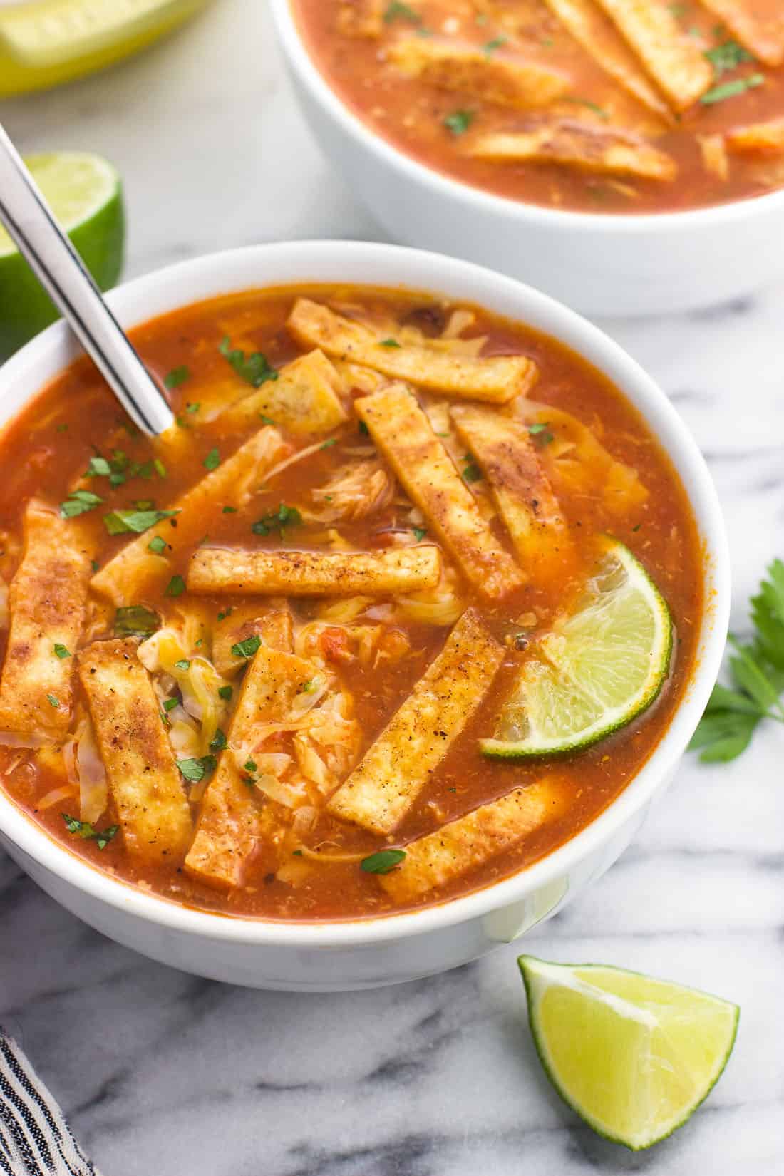 A bowl of soup topped with tortilla strips, shredded cheese, cilantro, and a lime wedge.