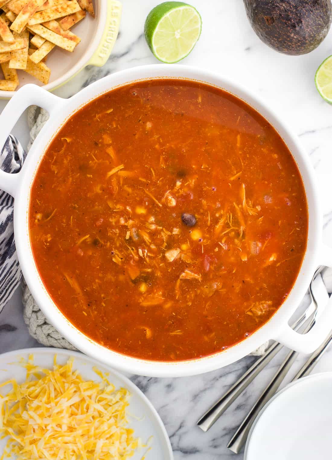 An overhead picture of a big pot of soup surrounded by plates of toppings.