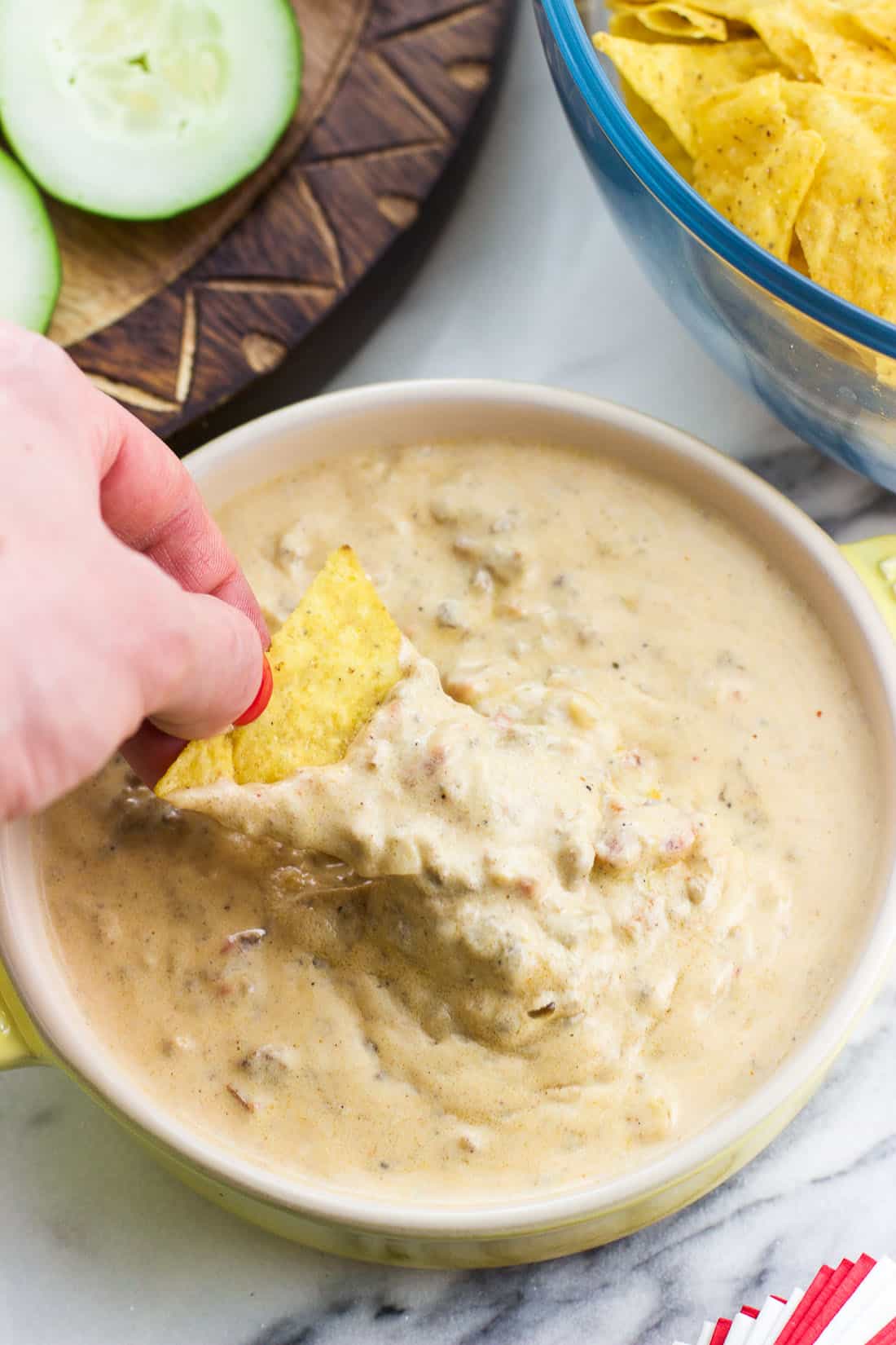 A hand dipping a tortilla chip into a bowl of beef queso dip.