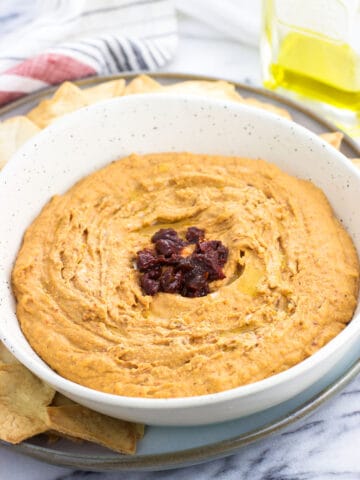 A bowl of hummus garnished with an olive oil drizzle and chopped up chipotle peppers