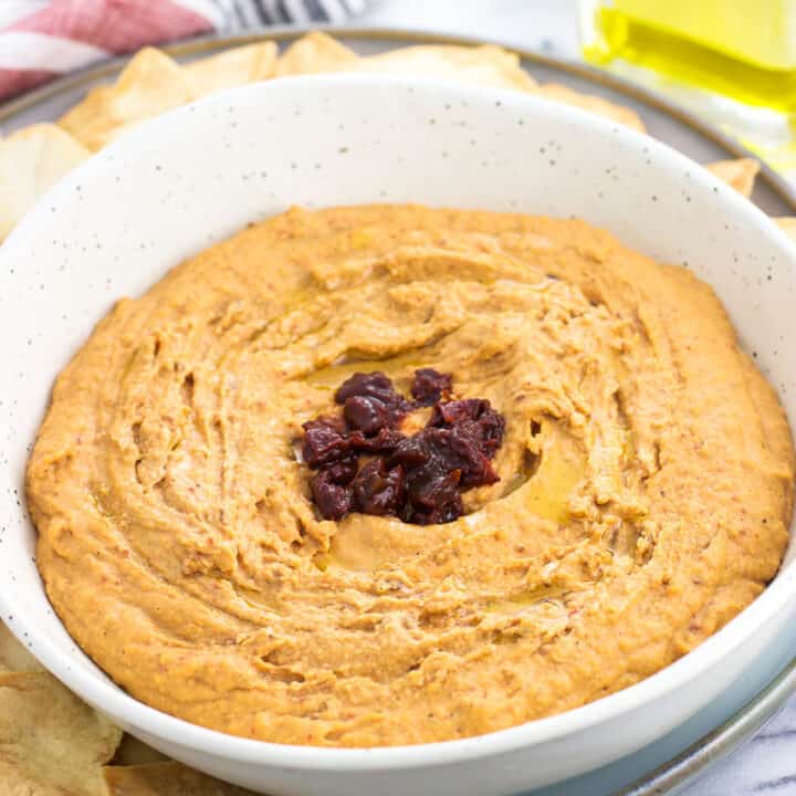 A bowl of hummus garnished with an olive oil drizzle and chopped up chipotle peppers