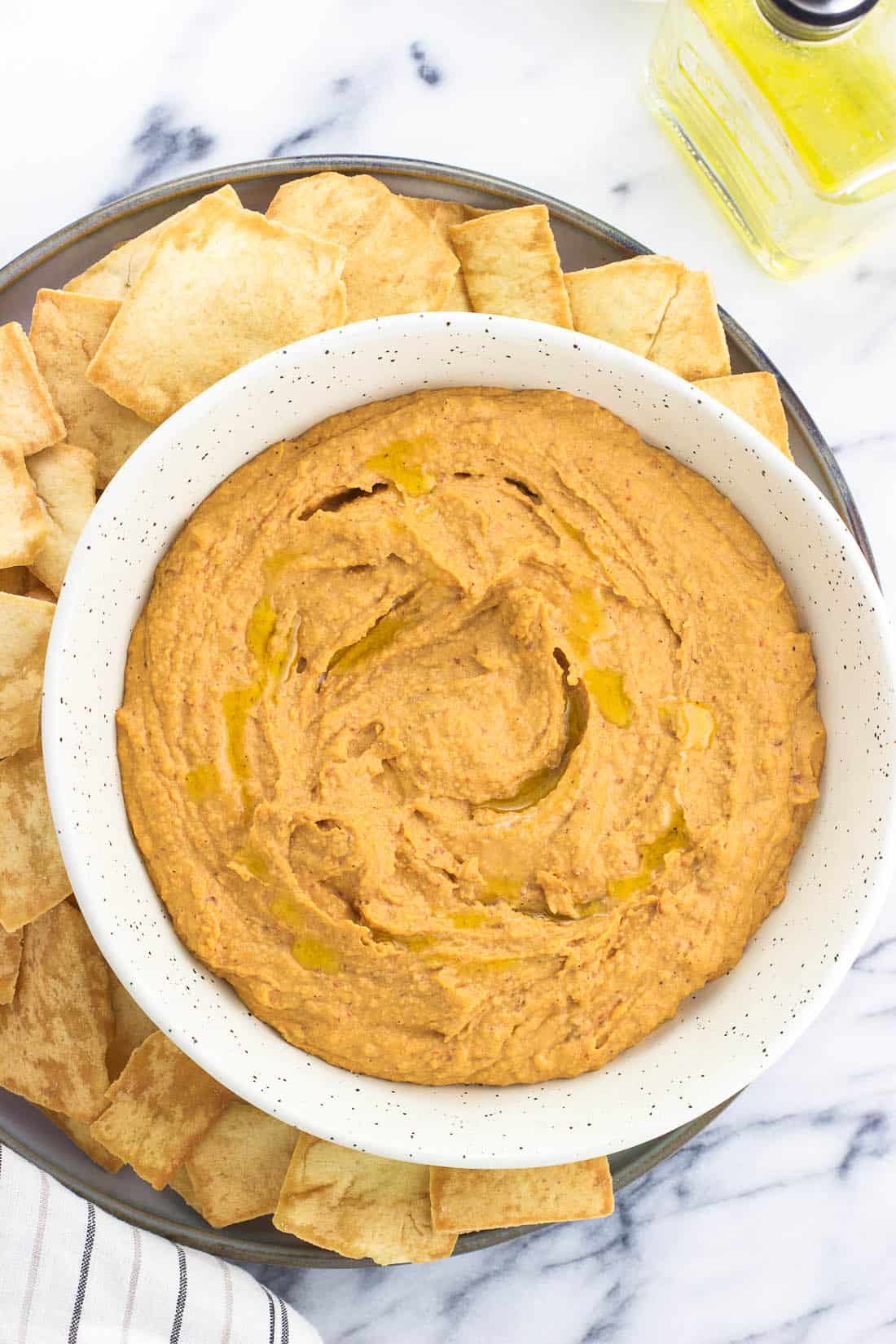 Hummus in a serving bowl on a large plate surrounded by pita chips