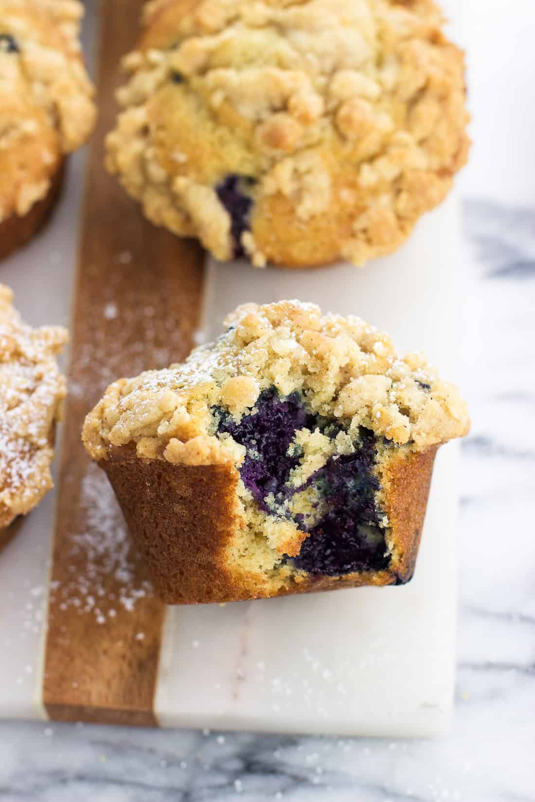 A muffin on a marble serving board dusted with powdered sugar with a big bite taken out of it