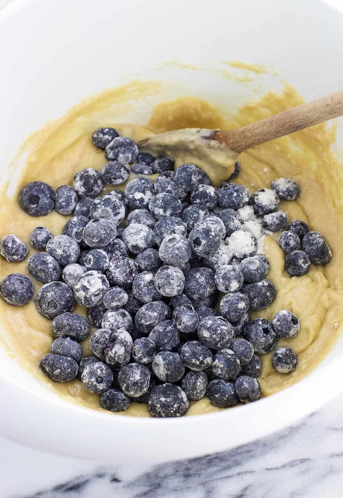 Flour-dusted fresh blueberries poured on top of muffin batter in a mixing bowl