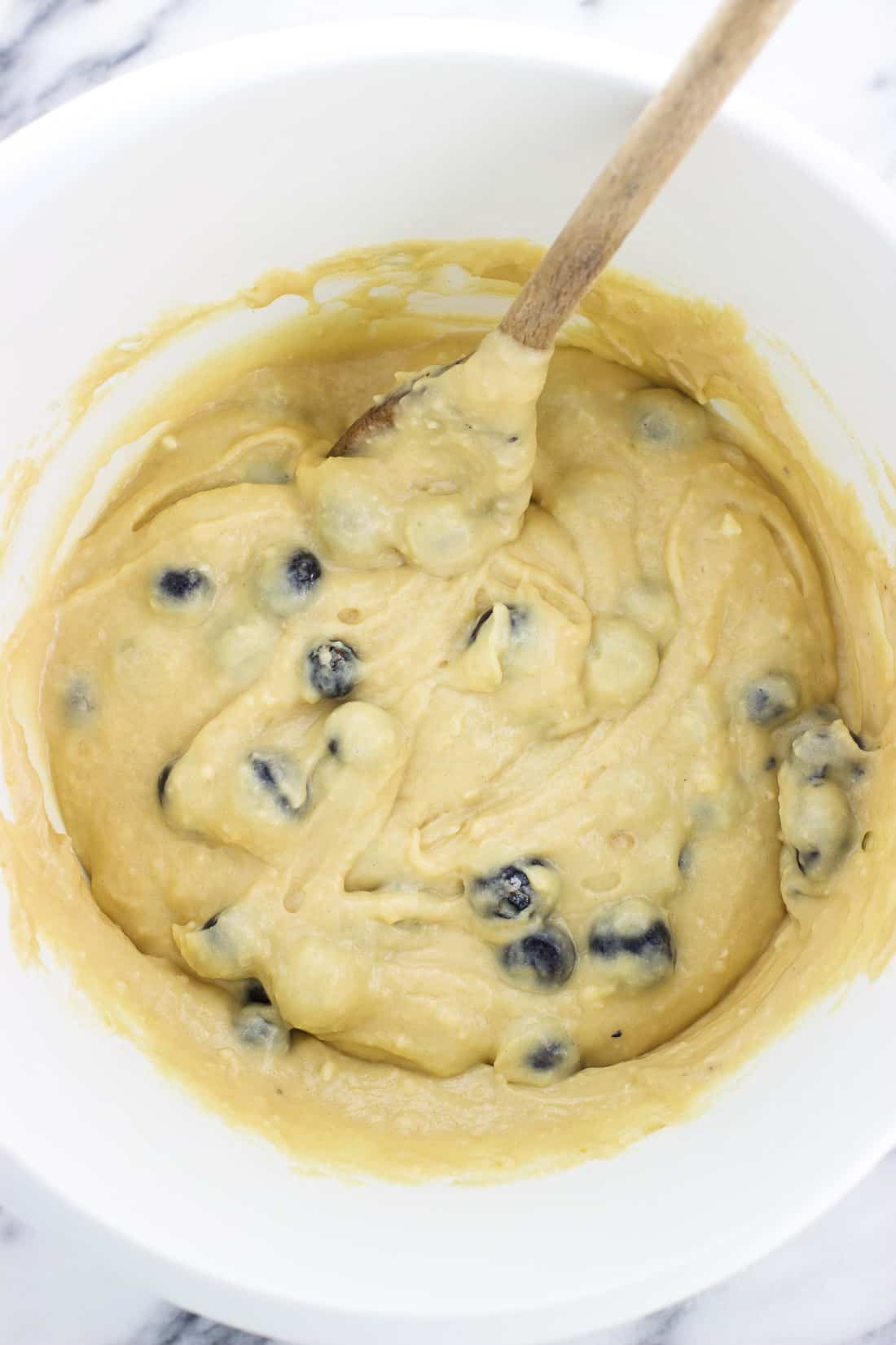 Blueberries stirred into muffin batter in a plastic mixing bowl