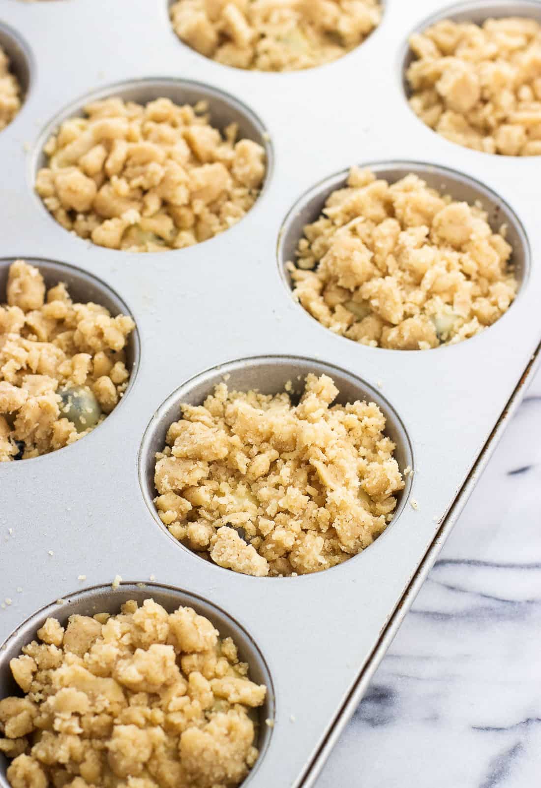 Muffin batter and crumble topping portioned out into a muffin tin before baking