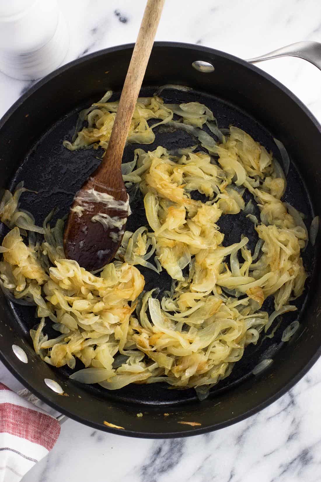 Fully caramelized onions in a pan with a wooden spoon