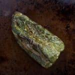 A roasted poblano pepper on a baking sheet.