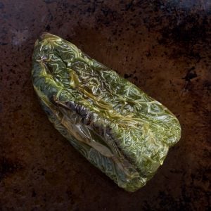 A roasted poblano pepper on a baking sheet.