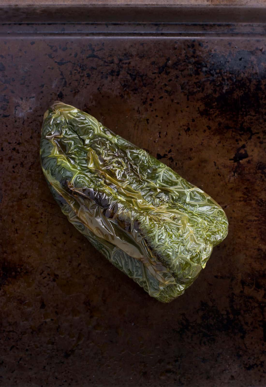 A roasted poblano pepper on a baking sheet.