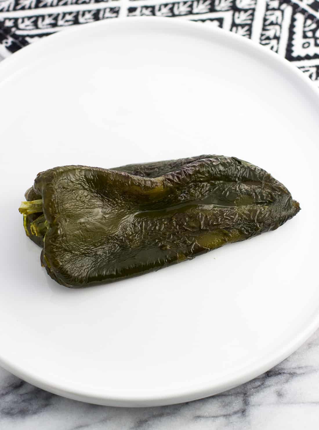 A roasted poblano pepper on a plate with the skin removed.