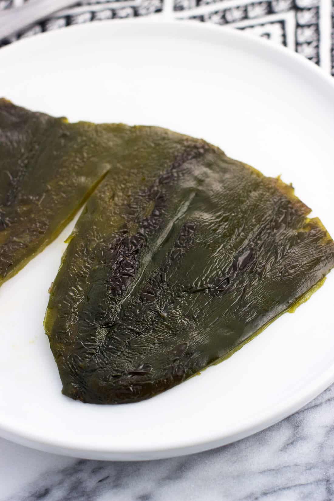A roasted poblano pepper sliced and deseeded to lay flat on a plate.