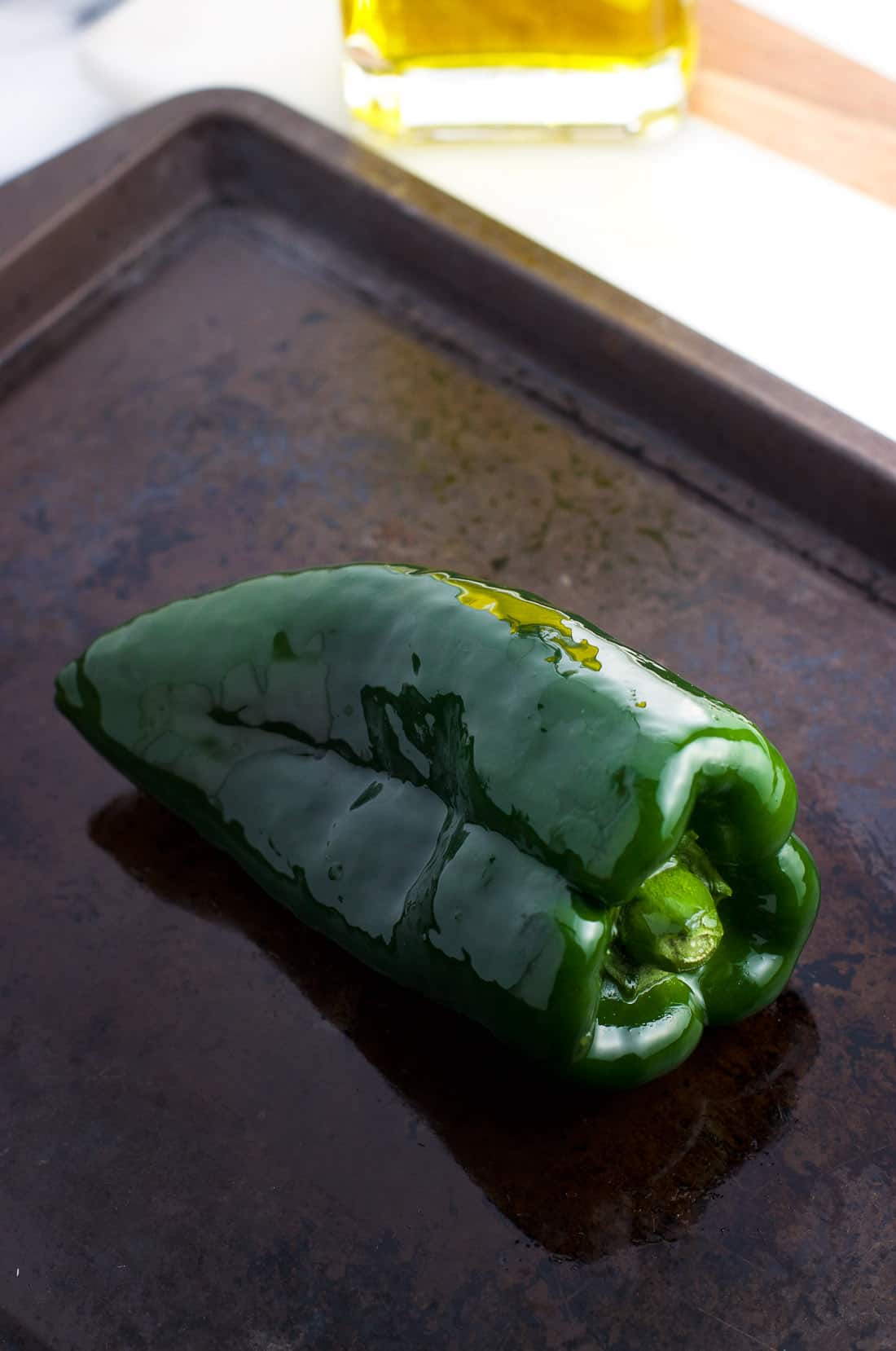 An oil-rubbed poblano pepper on a baking sheet.