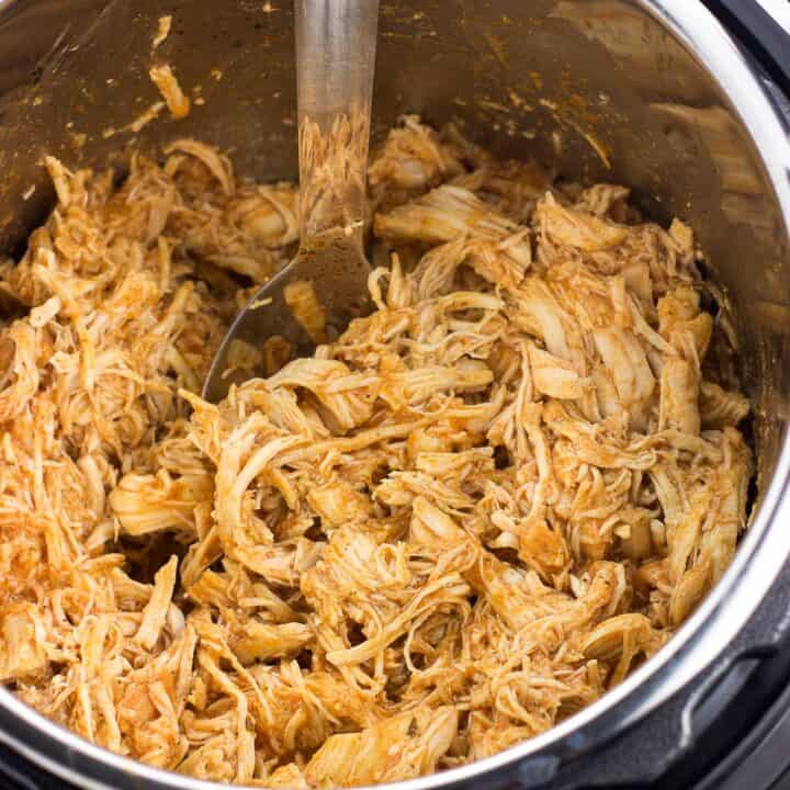 An Instant Pot filled with shredded buffalo chicken with a serving spoon.