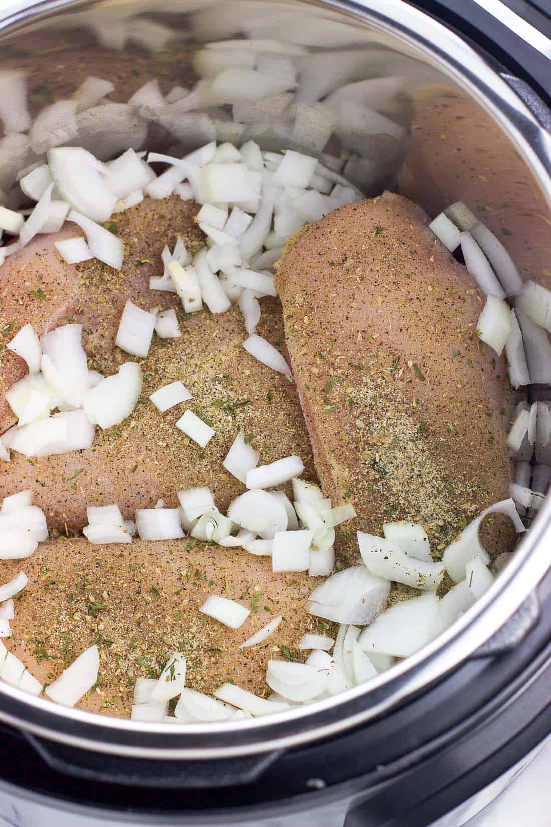 Raw chicken breasts, diced onion, and seasonings in the Instant Pot.