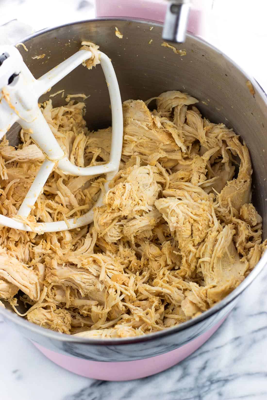 A metal stand mixer bowl filled with shredded chicken and the paddle attachment.