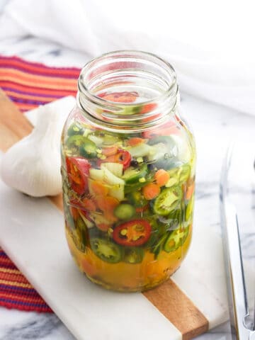 A large glass jar filled with pickled jalapeno, onion, and carrot slices and pickling liquid